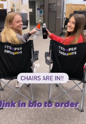 Two students sitting in chairs that are faced away from the camera. The students are holding water bottles and looking back at the camera. The following words are in the center of the image: The chairs are in