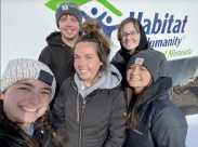 5 students in winter clothes posing in front of a habitat for humanity sign