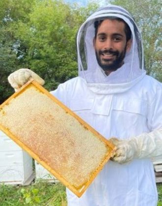 Sumit Mahajan posing in a bee suite holding a honeycomb tray