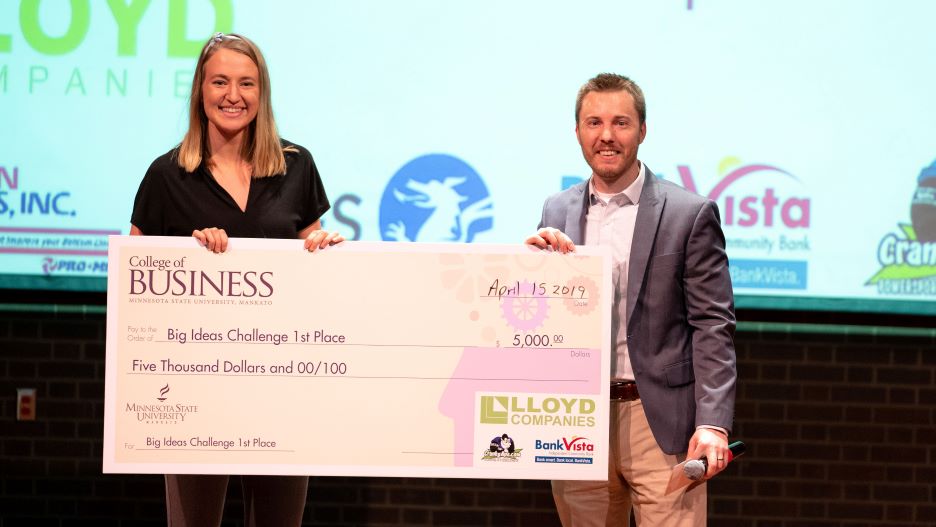 2 people holding a big check at an event of Collage of business studies