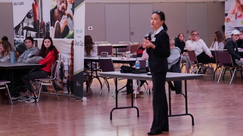 Ishuan Li Simonson standing up with a microphone during the SPARKTalk presentation at the 2025 Junior Achievement North Finance Park Mobile Days held in the CSU Ballroom