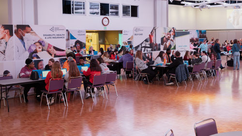 Groups of students sitting down at tables learning about financial education using the JA's simulation module software as volunteers walk around at the Junior Achievement North Finance Park Mobile Days held in the CSU Ballroom
