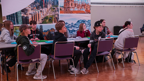 A group of students sitting at a table listening to instructions at the Junior Achievement North Finance Park Mobile Days held in the CSU Ballroom