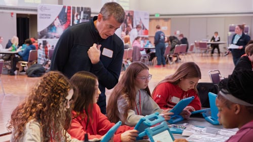 A volunteer helping a group of students sitting down at a table learning about the financial education using the JA's simulation module software at the Junior Achievement North Finance Park Mobile Days held in the CSU Ballroom