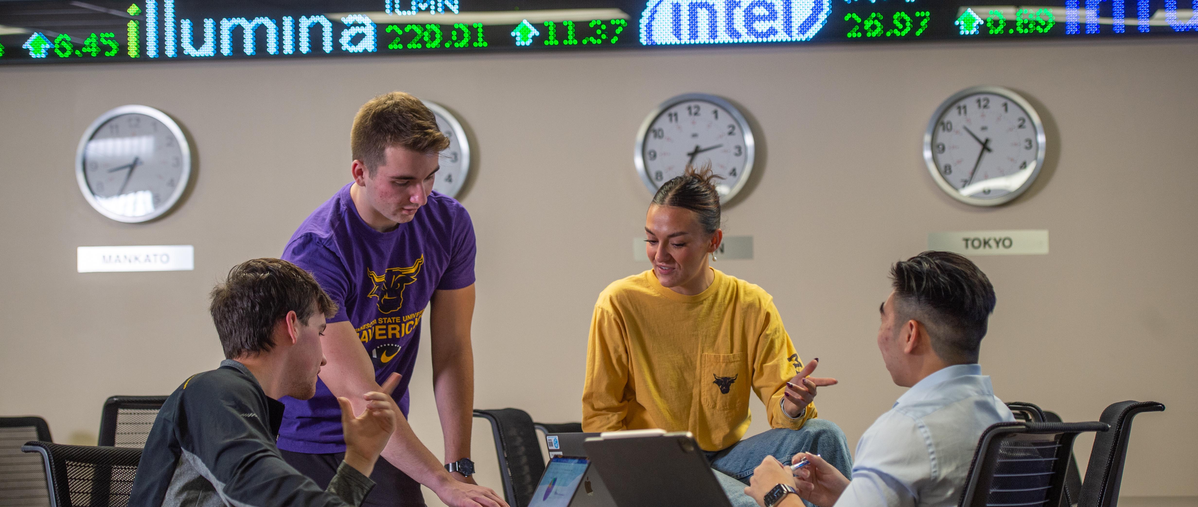 image of four students working together in front of the finance ticker